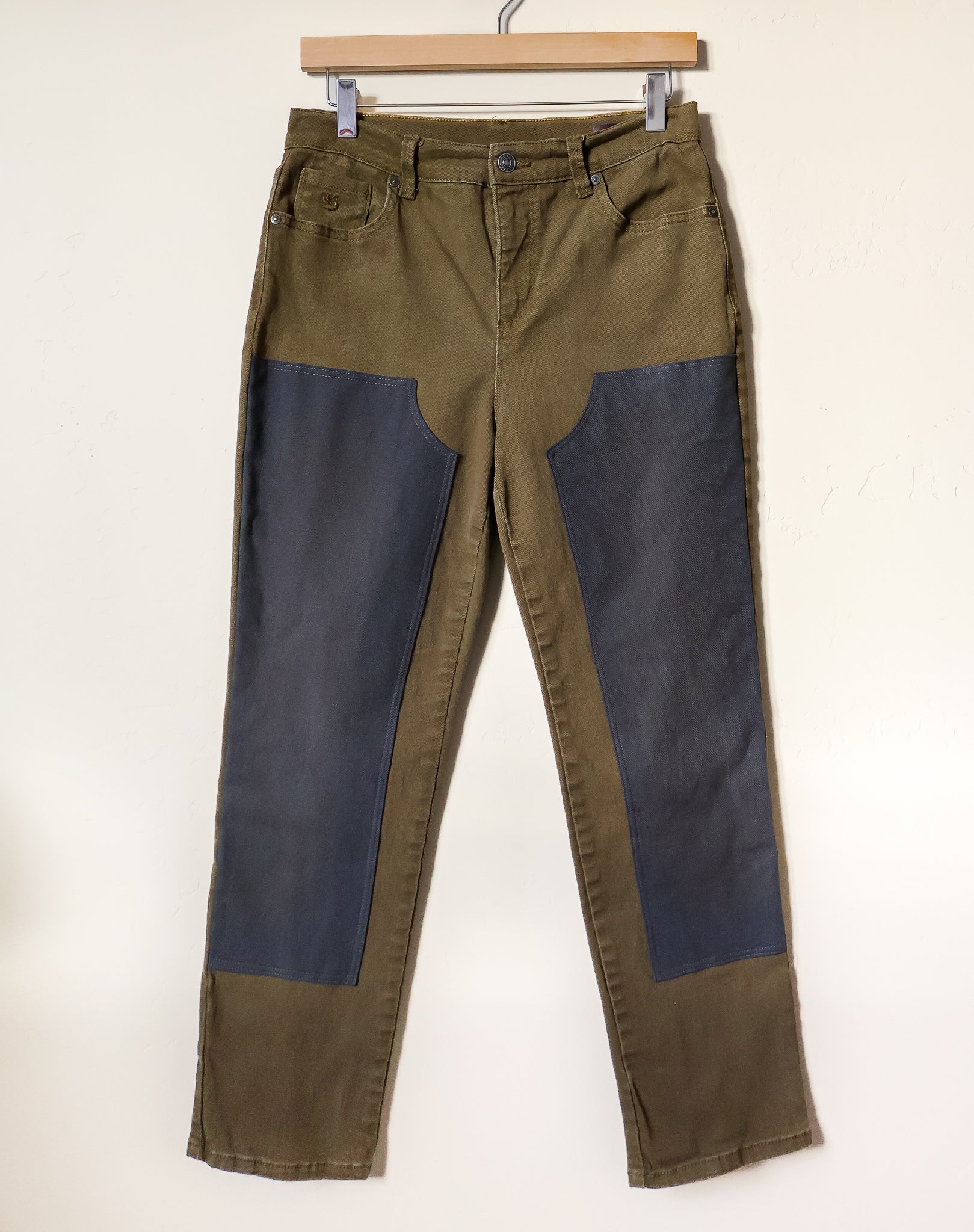 Pair of green and blue pants on a hanger against a white background